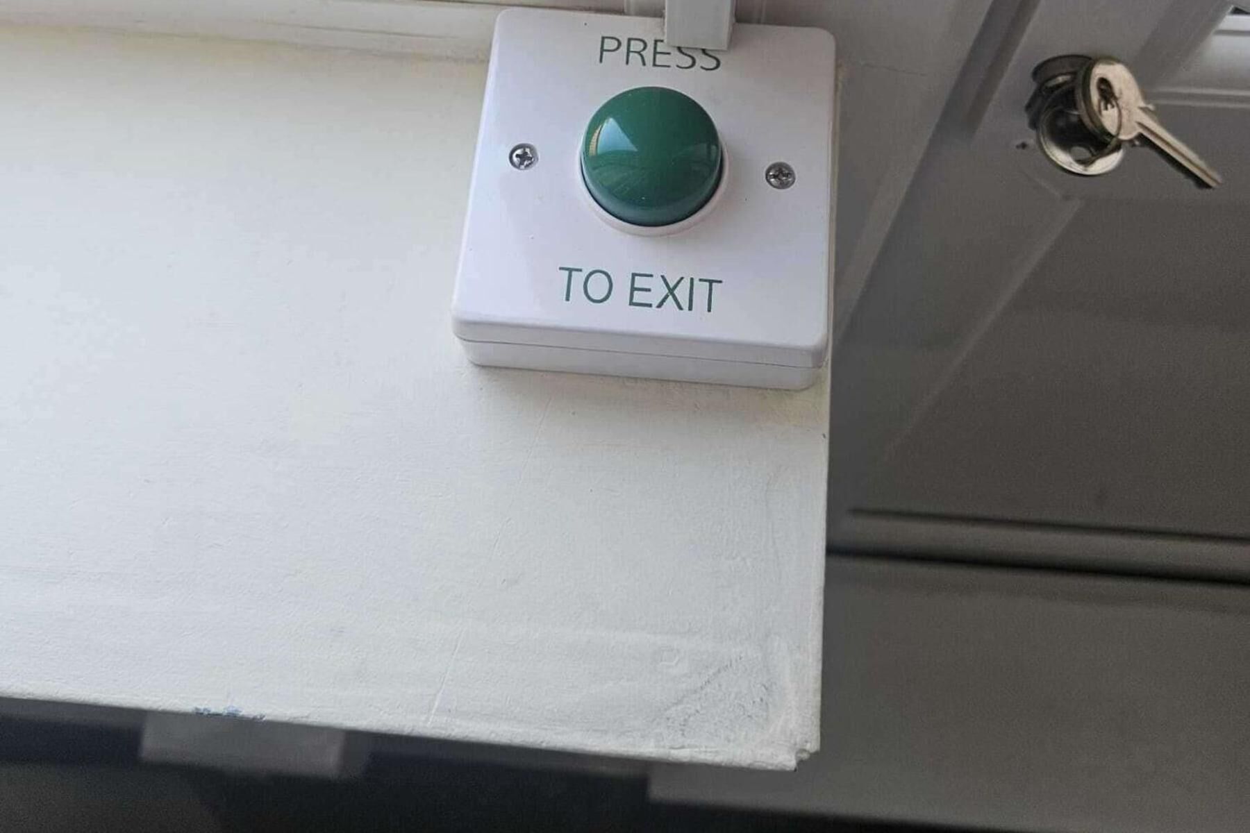 Een groene uitgangsknop op een witte achtergrond, met een sleutelgat in de buurt.