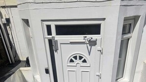 Una puerta blanca con un ventanal encima, una ventana pequeña a la derecha y un portón metálico a la izquierda.