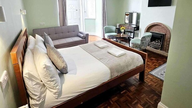 Una cama bien hecha con almohadas, un cabecero de madera y una pequeña alfombra sobre piso de madera.