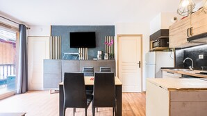 A modern kitchen with a flat-screen TV, wooden cabinets, and a dining area with a table and chairs.