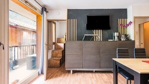 A modern kitchen with a flat-screen TV, wooden cabinets, and a dining area with a table and chairs.