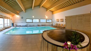 An indoor swimming pool with a wooden ceiling, a hot tub, and lounge chairs.