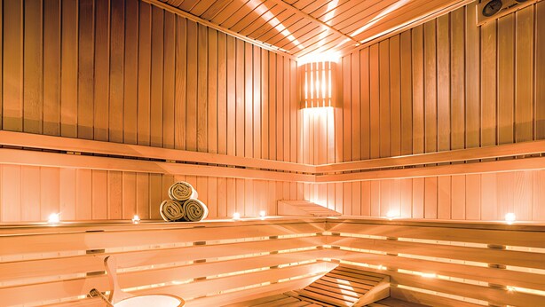 A sauna with wooden benches, a bucket, and a stack of towels.