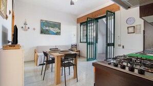 Una cuina amb fogó de gas, taula de menjador amb cadires, ventilador de sostre i un quadre a la paret.
