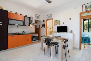 A modern kitchen with orange cabinets, a dining area with a table and chairs, a TV, and a window with a view.