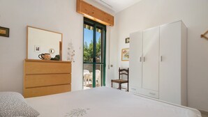 Un dormitori amb llit, prestatge, armari, cadira i finestra amb vistes.