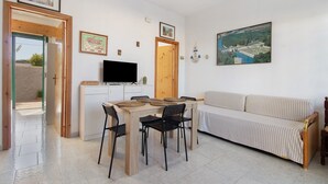 Un saló amb un sofà, una taula de dinar amb cadires, una televisió i un quadre a la paret.