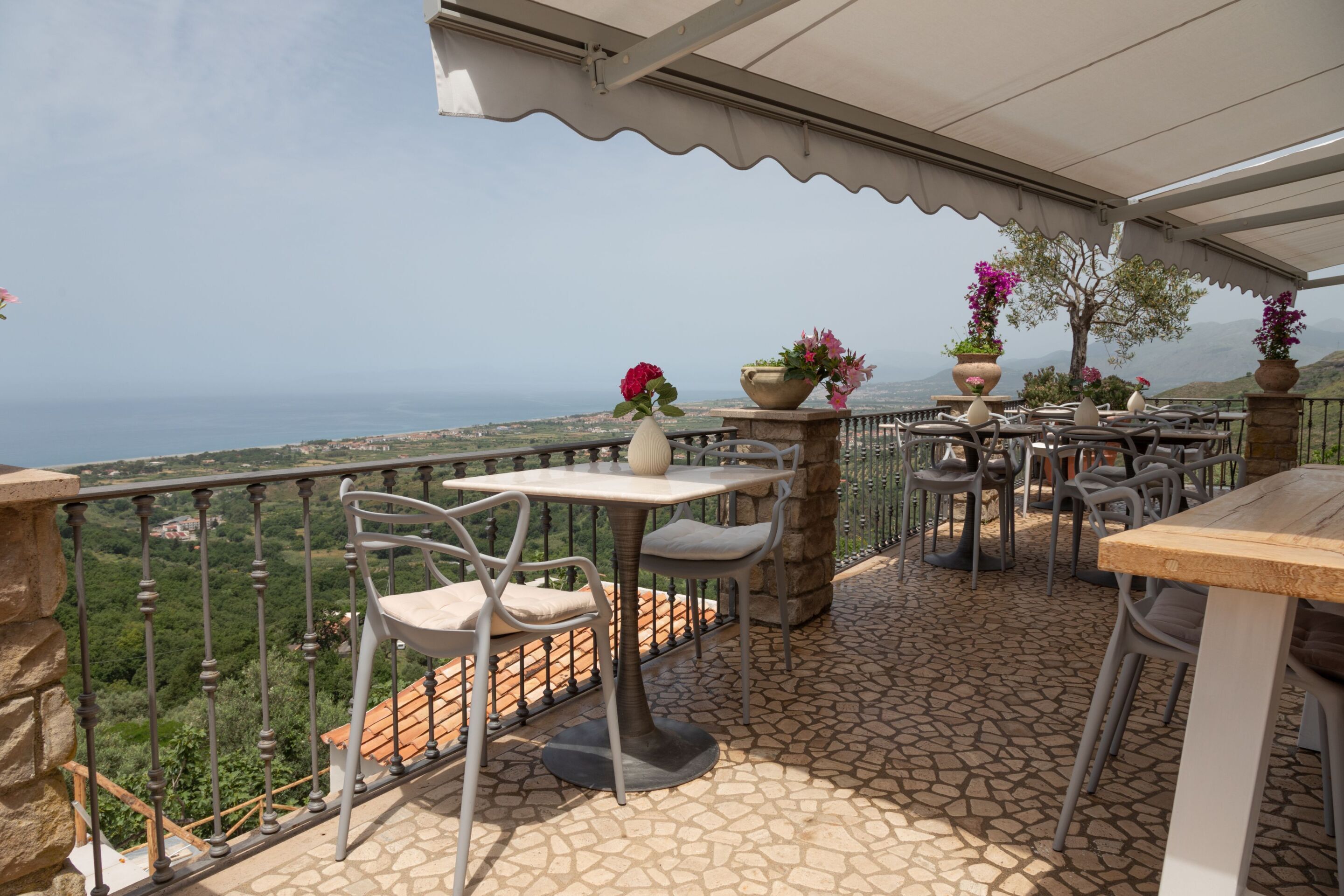 Terraza exterior con suelo de piedra, barandales de metal y mesas con sillas.