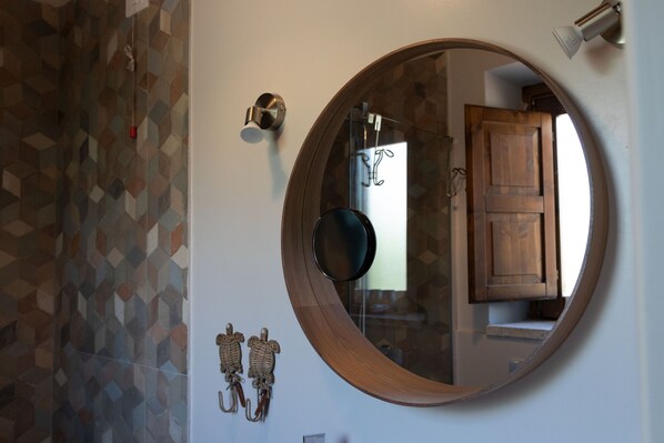 Un baño con un espejo redondo, baldosas de diseño geométrico, una puerta de madera y un perchero para toallas.