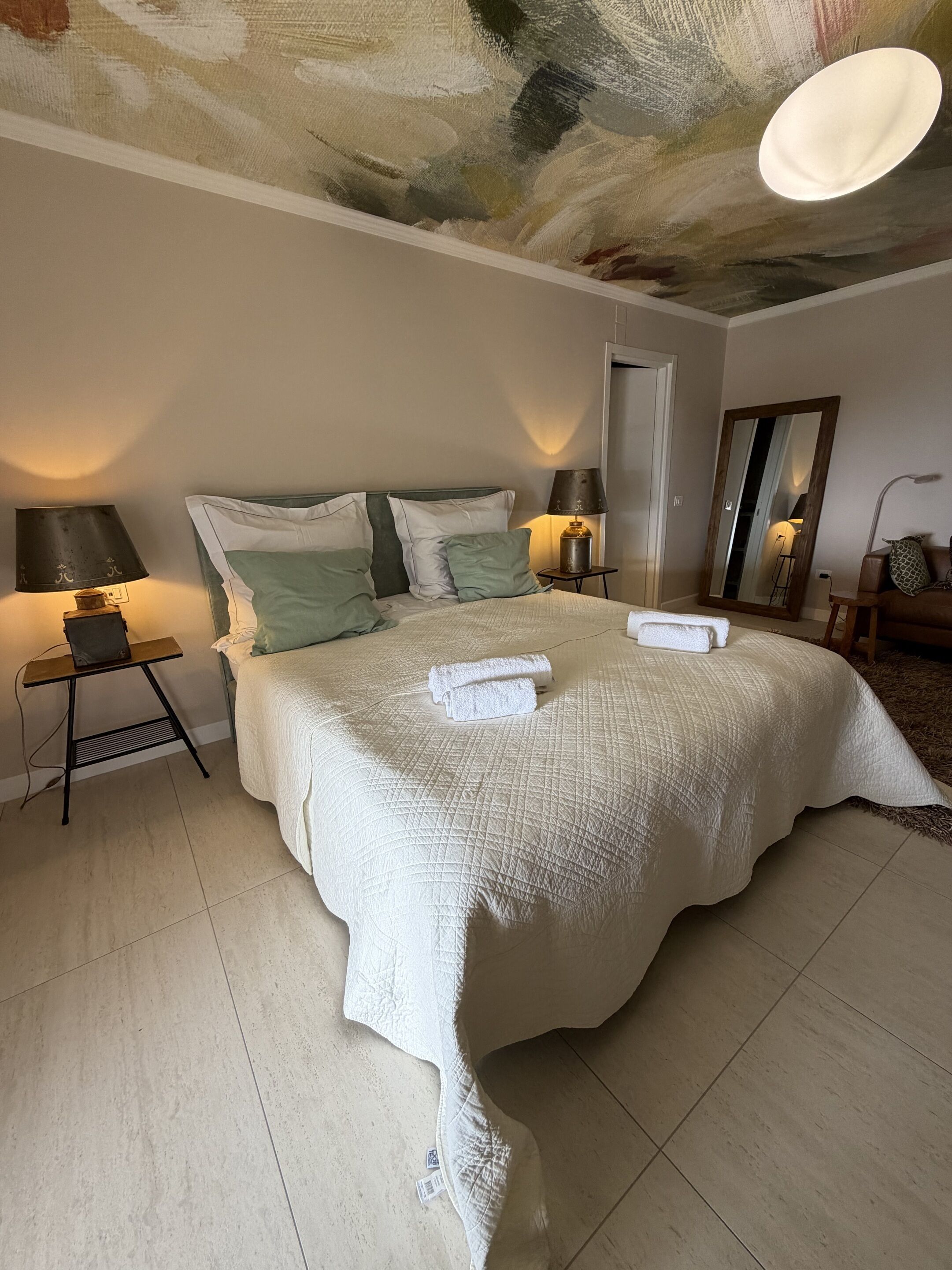 Un dormitorio con una cama grande, dos lámparas de noche, un espejo y una puerta.