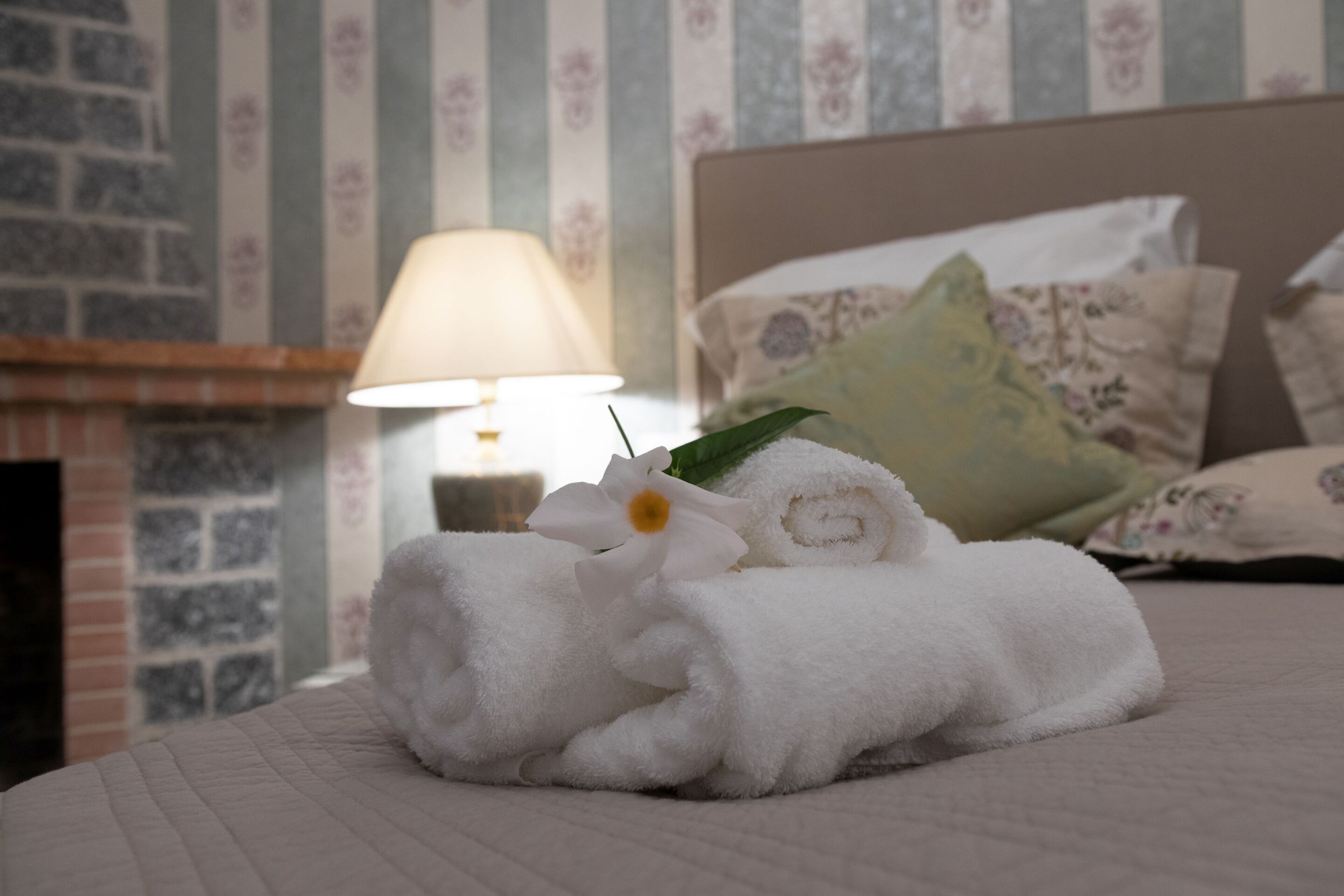 Ein ordentlich bezogenes Bett mit aufgerollten weißen Handtüchern und einer einzelnen weißen Blume.