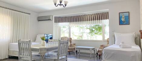 A hotel room with a dining area, a bed with a blue accent, a ceiling fan, and a window with curtains.