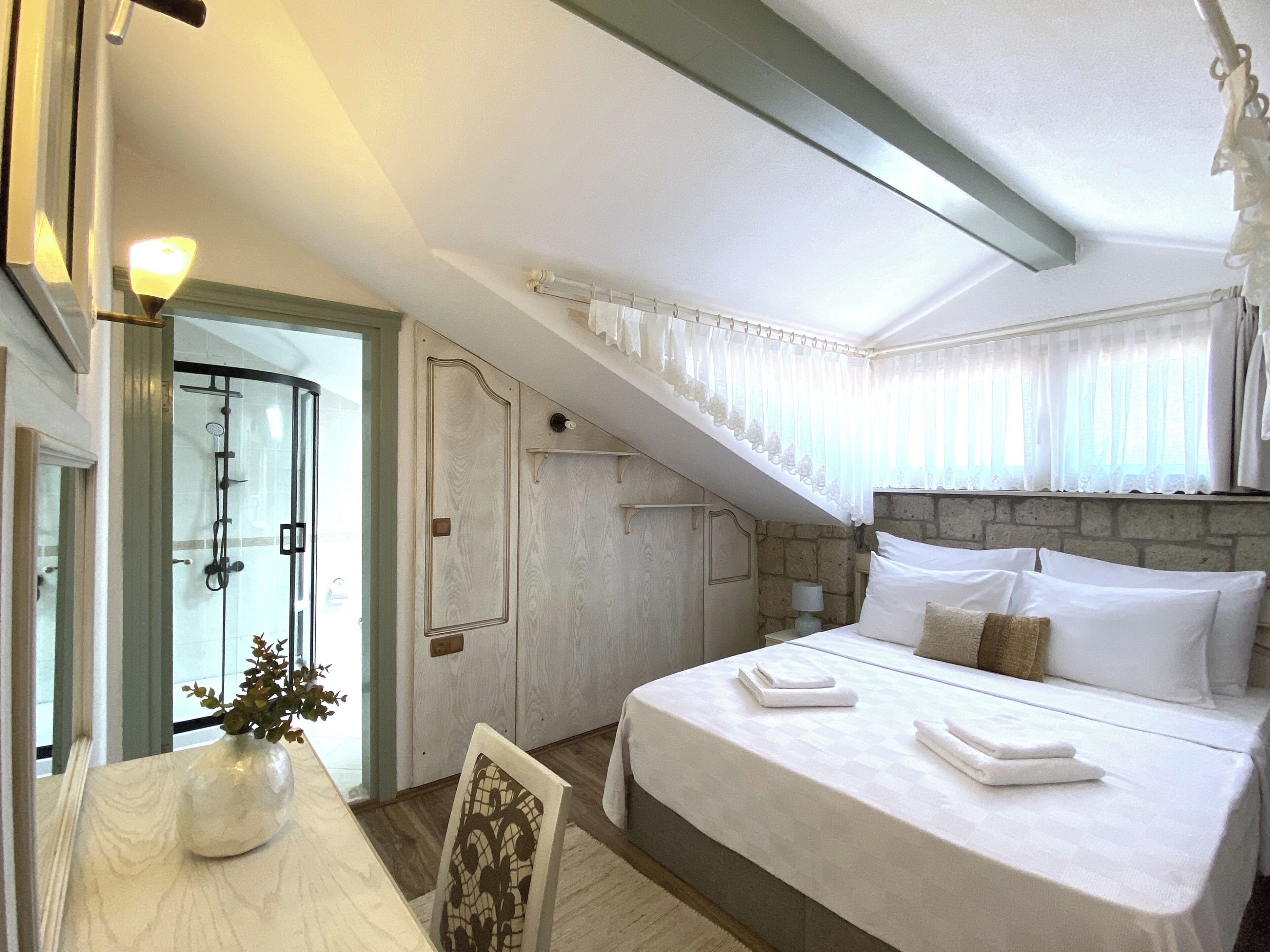 A bedroom with a bed, a nightstand, a vase with flowers, and a staircase leading to an upper level.