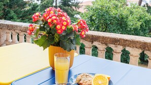 Een tafel met een glas sinaasappelsap, een bord met een koekje en een sinaasappelschijfje, en een potplant met rode bloemen.