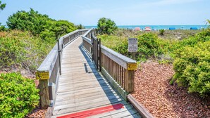 Une promenade en bois mène à une zone de plage où des panneaux indiquent les commodités disponibles, comme des clubs de plage, des piscines et une rivière à courant doux.