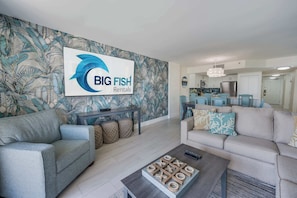 A modern living room with a large sofa, a coffee table, and a wall-mounted sign for Big Fish Rentals.