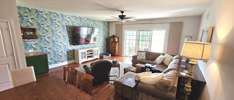 A living room with a TV, sofa, chairs, and a wooden cabinet.