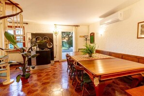 Zona pranzo con tavolo e sedie in legno, una scala a chiocciola e angolo cottura con frigorifero e lavello.