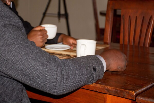 A person sitting at a wooden table with a white mug and a plate. - Destination 3 Degrees Hotel (Arusha)