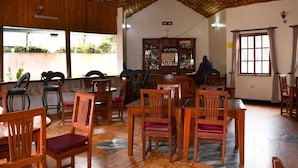 Un restaurant avec des tables et des chaises en bois, un bar avec des étagères remplies de bouteilles, et une vue dégagée grâce à de grandes fenêtres.