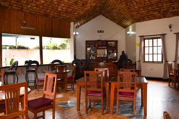Un ristorante con tavoli e sedie in legno, un'area bar con scaffali pieni di bottiglie e una vista attraverso ampie finestre.