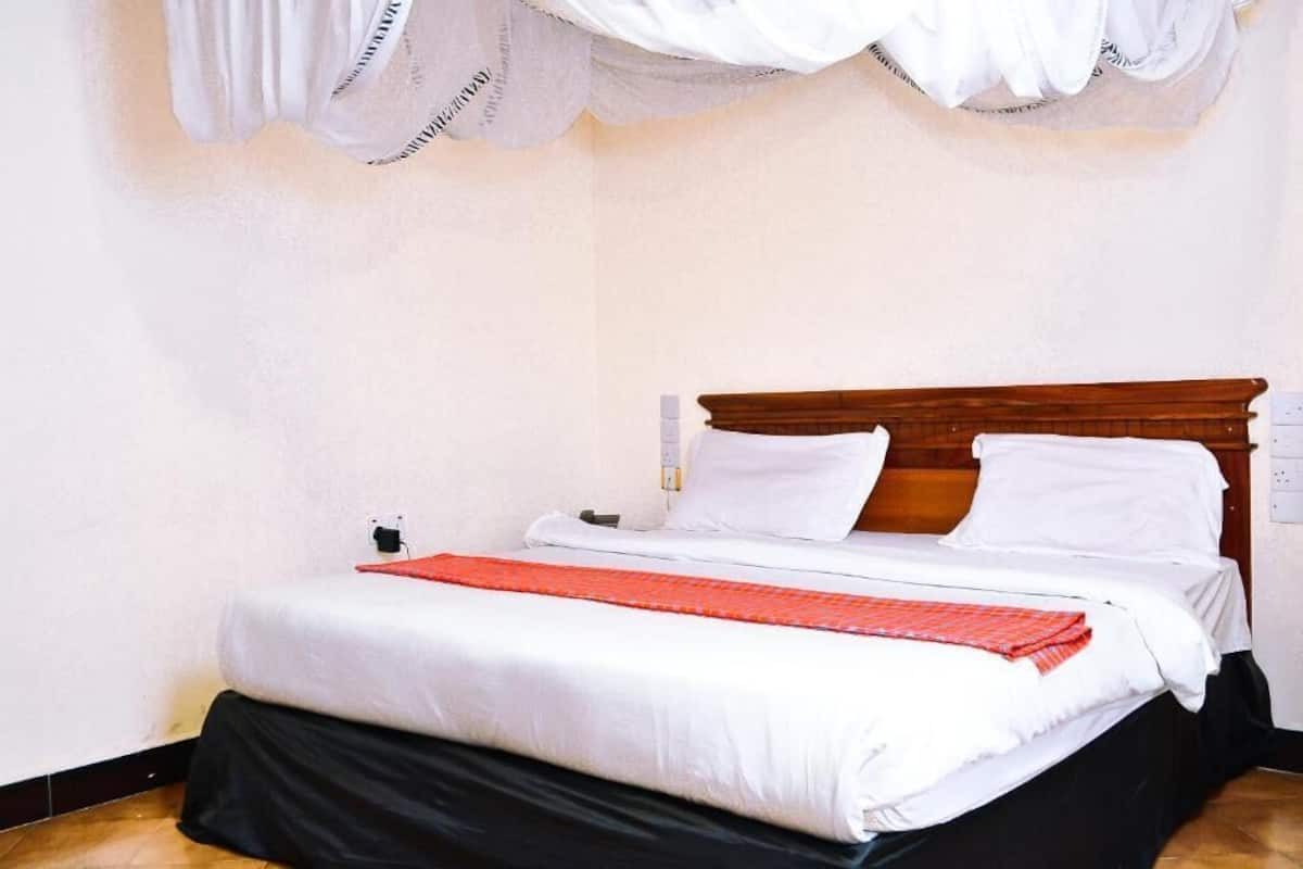 A neatly made bed with white linens and a red blanket, a wooden headboard, and a white curtain.