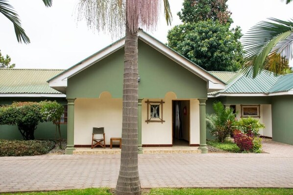 A two-story building with a green facade, a covered entrance with a bench, and a palm tree in the foreground. - Destination 3 Degrees Hotel  (Arusha)