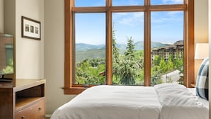 Un dormitorio con un ventanal que ofrece vistas a un paisaje montañoso y un edificio.