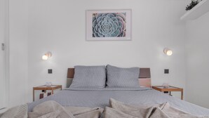 Uma cama bem arrumada com roupa de cama estampada, duas mesas de cabeceira com luminárias e uma obra de arte emoldurada na parede.