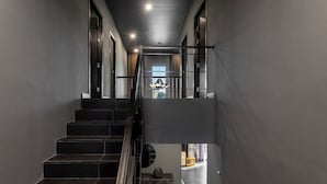 Una escalera moderna con barandilla de metal que conduce a un rellano en el segundo piso con vistas al exterior.