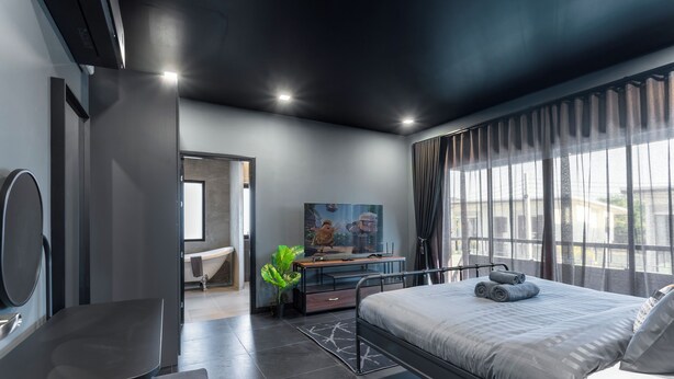 Una habitación de hotel moderna con una cama, un escritorio, una silla, un televisor y un amplio ventanal con cortinas.