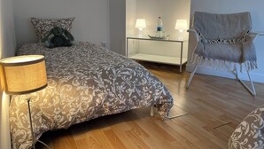 Une chambre à coucher avec une couvre-lit à motifs, une lampe de chevet, une chaise et une table en verre avec deux lampes.