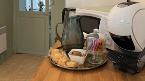 Un coin cuisine comprenant une machine à café, un pichet, un plateau de pâtisseries et une cafetière sur une table en bois.