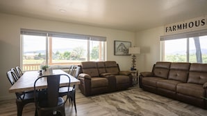 Amplia sala de estar con una mesa de comedor, dos sofás y ventanas grandes que ofrecen vistas al exterior.
