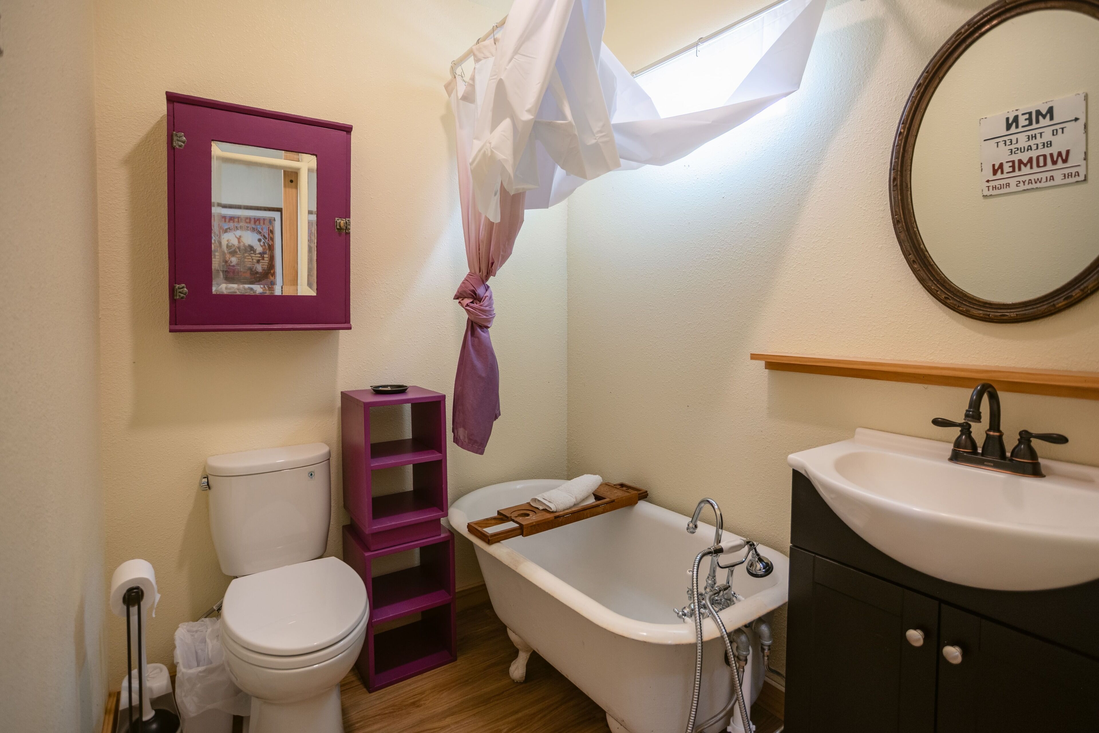 A bathroom with a white toilet, a wooden shelf, a white bathtub, and a sink.