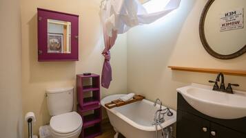 A bathroom with a white toilet, a wooden shelf, a white bathtub, and a sink.