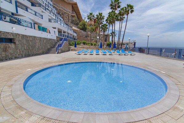 Un área de piscina con sillas de descanso, un muro de piedra y un edificio con balcones.