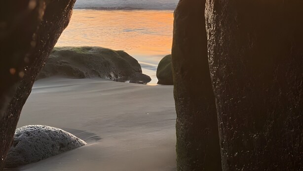 A sunset view through a rock formation with a beach and ocean in the background. - Stunning Sunset Ocean View Vacation – Ocean Views, Shared Pool & Wi-Fi (Taurito)