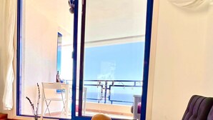 A room with a large window, a sofa, a small table, and a decorative vase. - Stunning Sunset Ocean View Vacation – Ocean Views, Shared Pool & Wi-Fi (Taurito)
