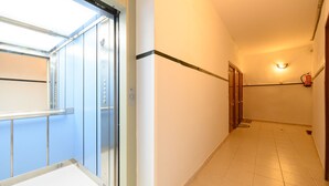 A hallway with a glass elevator door, a fire extinguisher mounted on the wall, and a tiled floor. - Monthly Rental in Madrid - Modern 1 bedroom flat (Madrid)
