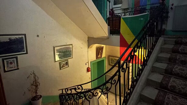 Una escalera con barandilla de hierro forjado negro, una puerta verde y un muro colorido.