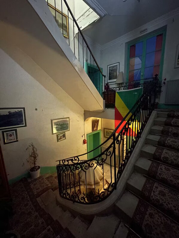 A staircase with a black wrought iron railing, a green door, and a colorful wall.