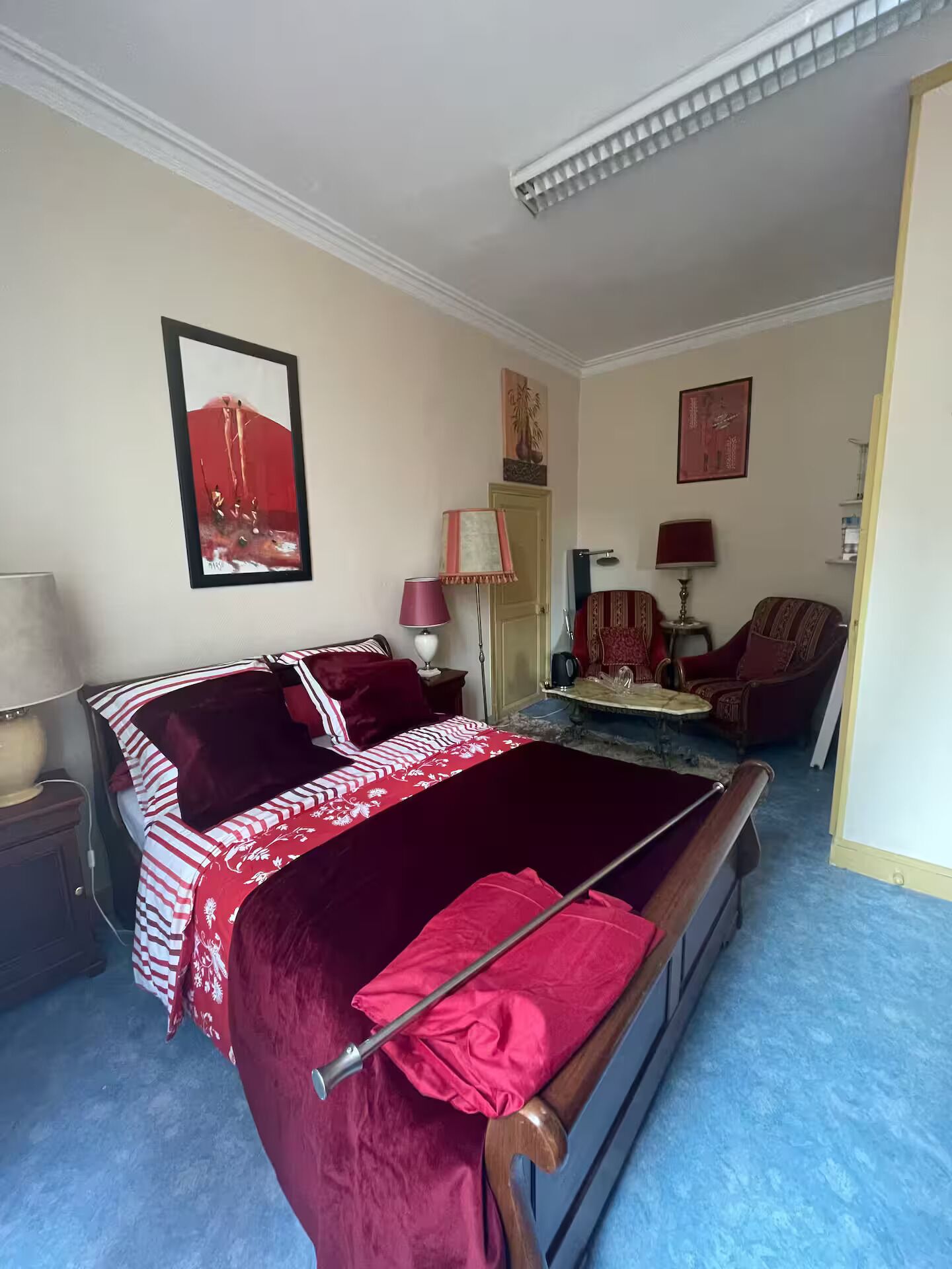 A bedroom with a bed, a chair, a lamp, and a painting on the wall.