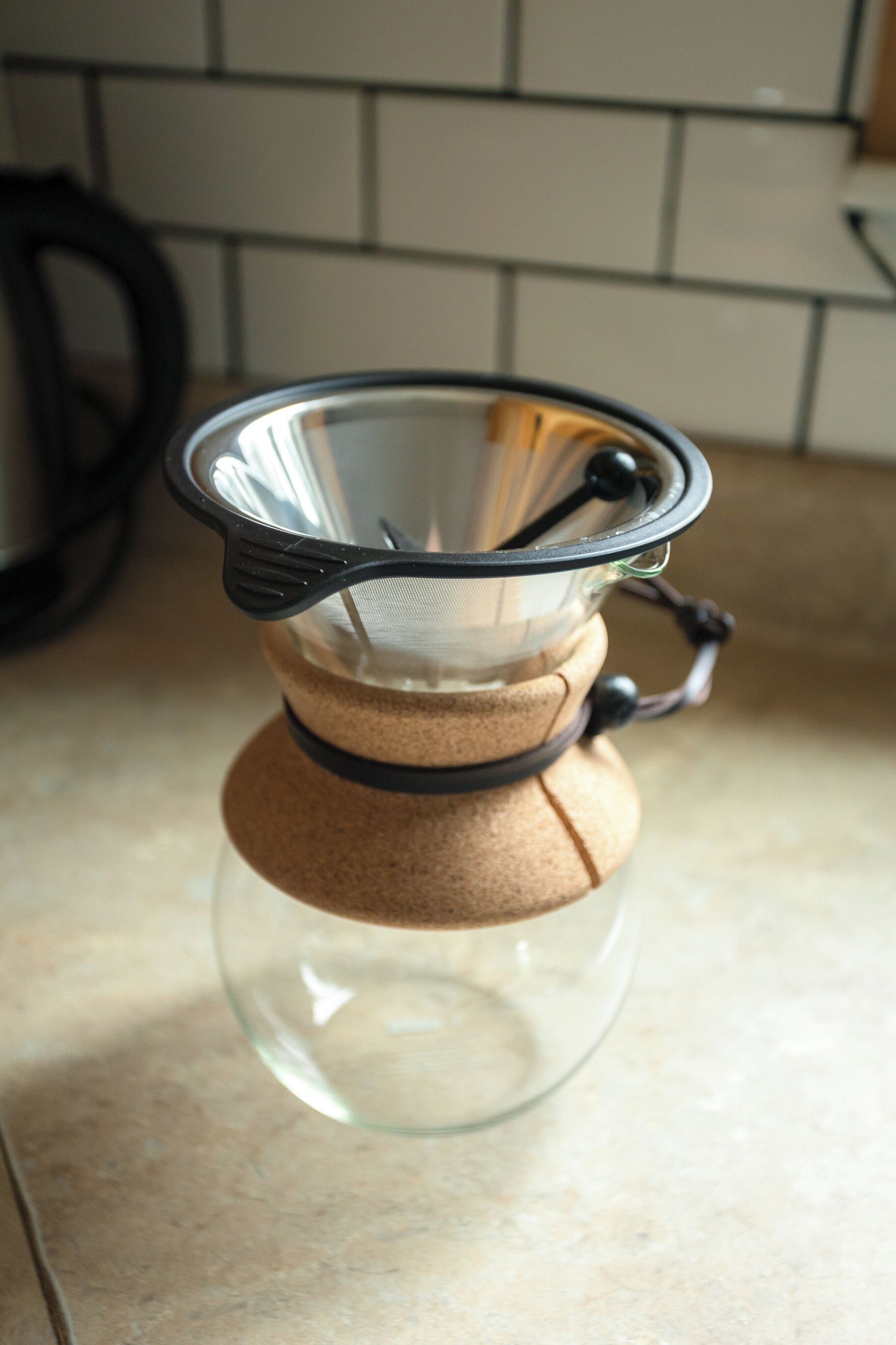 Een koffiezetter met een metalen filter en een bruin papieren filter, geplaatst op een glazen kan.