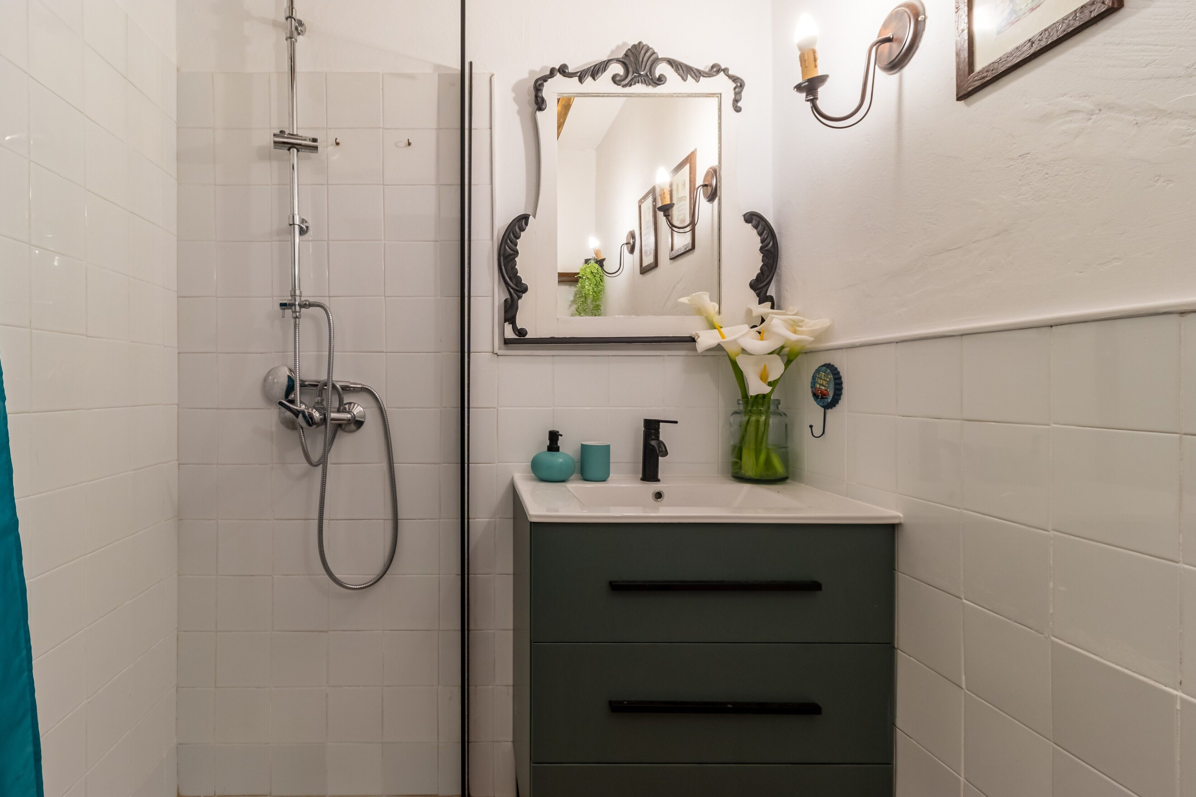A bathroom with a shower, a sink with a mirror, and a vase with flowers.