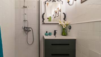 A bathroom with a shower, a sink with a mirror, and a vase with flowers.