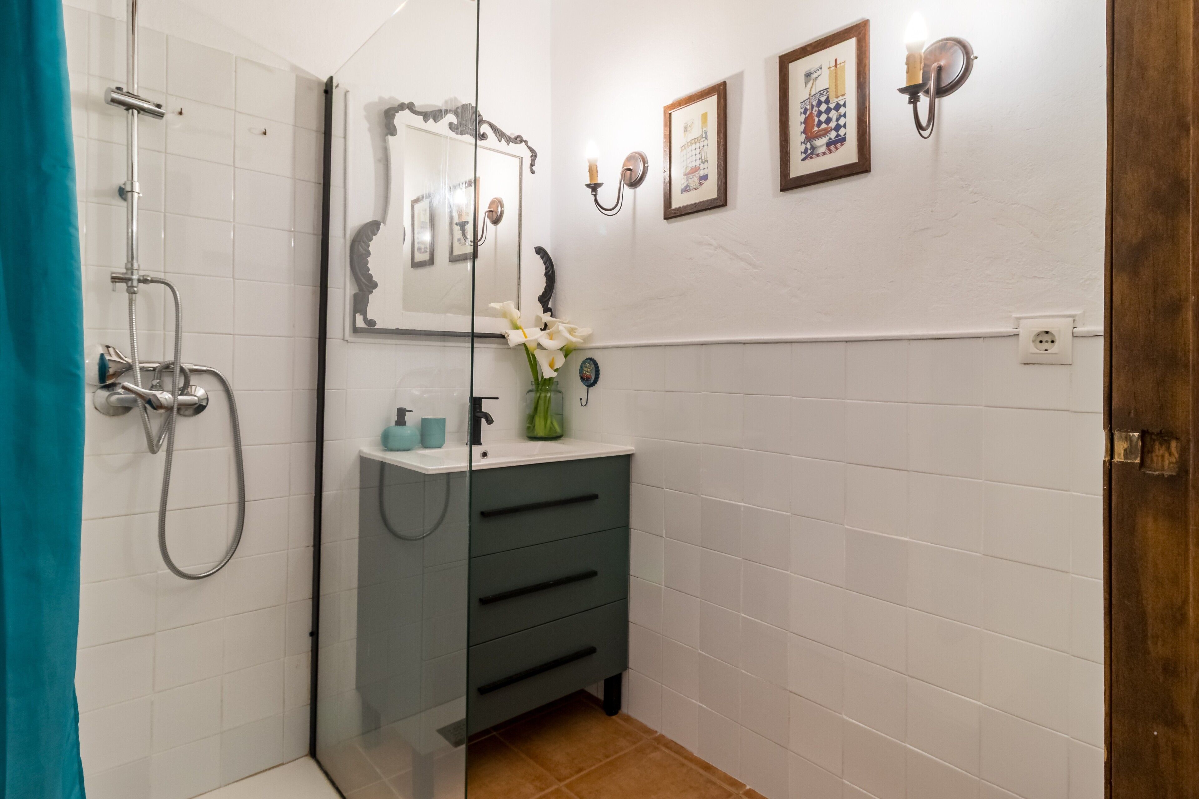 Een badkamer met een douche, een wastafel met spiegel en een bloemenvaas.