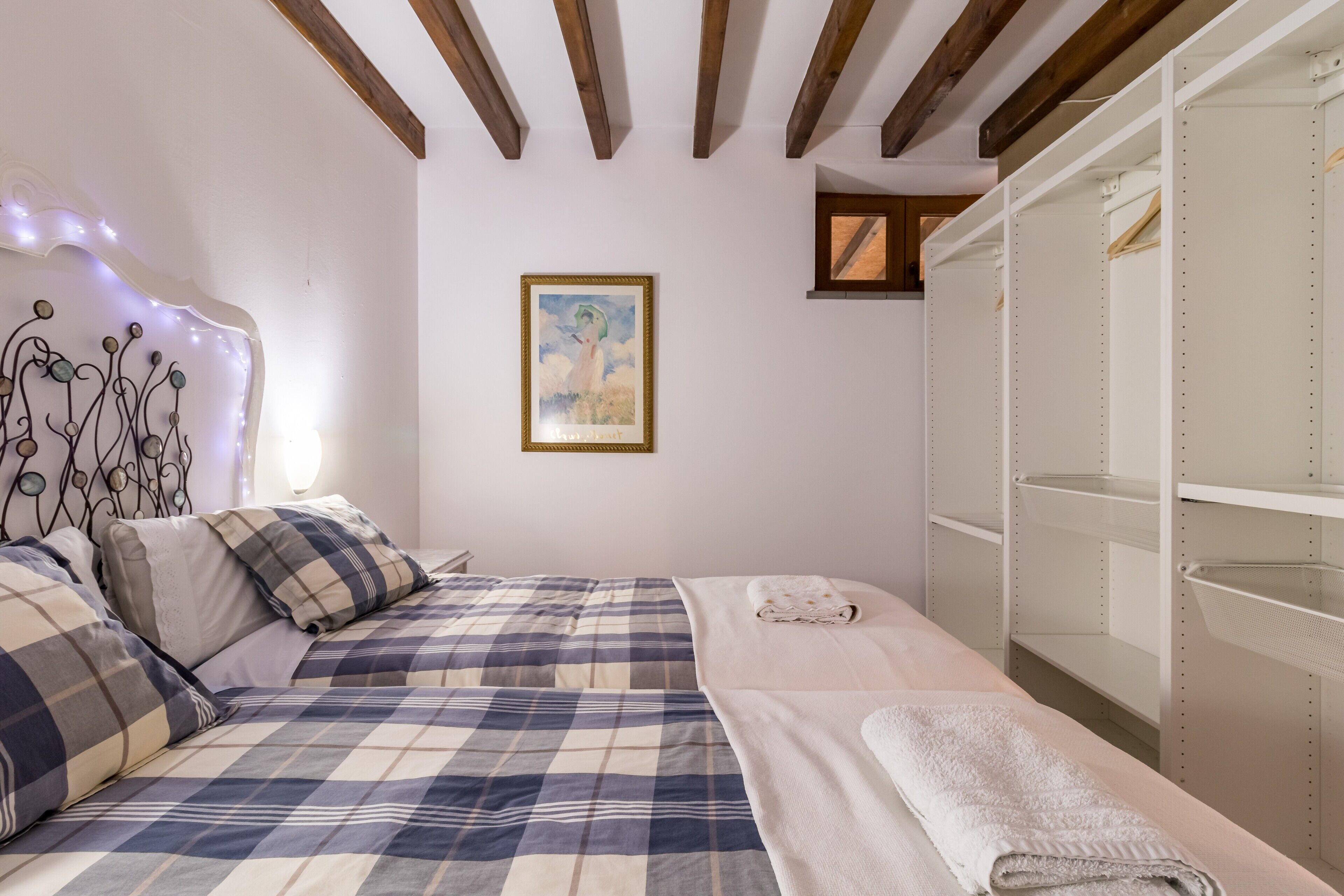 A bedroom with two beds, a wall-mounted shelf, and a framed painting.