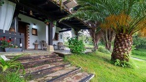 Una casa tradicional con una escalera de piedra que lleva a un porche, rodeada de follaje y palmeras.