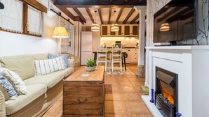 Una sala de estar con sofá, mesa de centro, chimenea, televisor, zona de cocina y mesa de comedor.